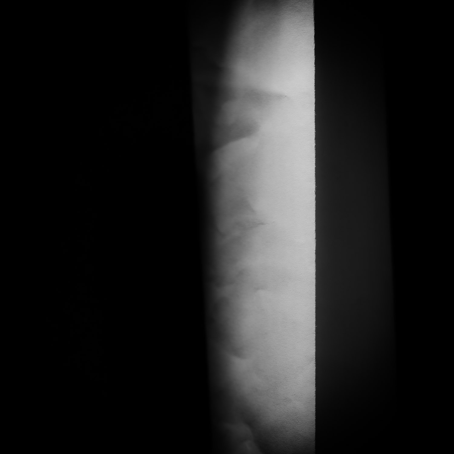 abstract minimal black and white photograph showing a vertical illuminated surface next to a deep shadow area with soft structural gradients